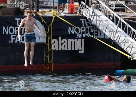 Brooklyn, Usa. August 2024. Beim North Face Climb Festival am Pier 5 im Brooklyn Bridge Park in New York City springt ein Kletterer ins Wasser. Die North Face Company veranstaltete ein Climb Festival im Brooklyn Bridge Park Credit: SOPA Images Limited/Alamy Live News Stockfoto