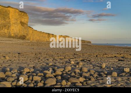 Die Steine und die Klippen von Llantwit Major Strand in der Abendsonne mit einigen Wolken über die Klippen, South Glamorgan, Wales, Großbritannien Stockfoto