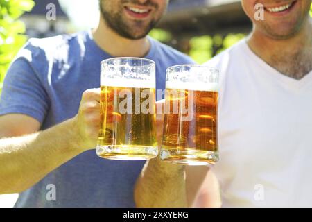 Nahaufnahme von zwei jungen Männern in Freizeitkleidung, die eine Brille mit Bier ausstrecken und im Freien lächeln Stockfoto