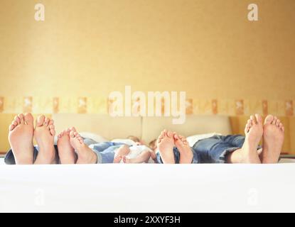 Süße Familie im Bett. Vater, Mutter und drei kleinen Kindern, in der Nähe auf den Füßen Stockfoto