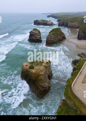 Wellen schlagen gegen große, grasbewachsene Felsen entlang einer steilen, zerklüfteten Küste, aus der Vogelperspektive, Praia das Catedrais, Playa de las Catedrales, Cathedra Stockfoto