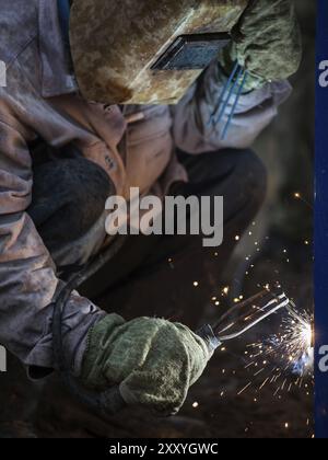 Schwere Industrie Schweißgerät Arbeiter in Schutzmaske Hand arc Schweißbrenner arbeiten auf Metall Bau Stockfoto