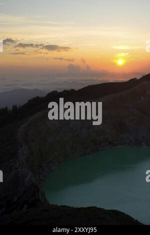 Die Morgensonne steigt über einem Wolkenmeer im Kelimutu-Nationalpark auf und offenbart einen grünen vulkanischen See Stockfoto