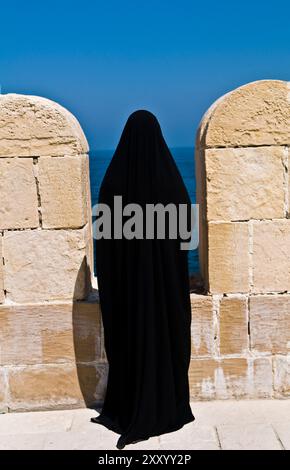 Eine ägyptische Frau in schwarzer Abaya mit Blick auf das Meer von Fort Qaitbey in Alexandria, Ägypten. Stockfoto