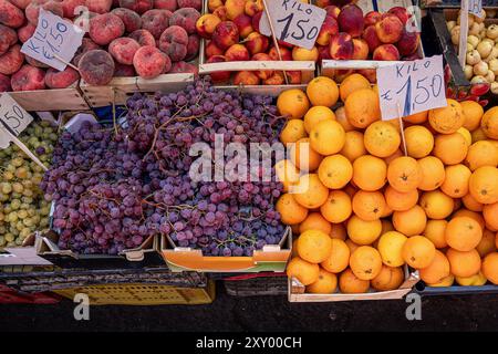 Lebendige Präsentation von frischem Obst am italienischen Marktstand. Reife Pfirsiche, Nektarinen, violette Trauben und Orangen in Holzkisten. Preisschilder in Euro sh Stockfoto