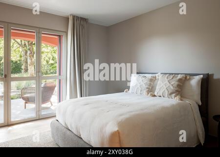 Innenraum eines kleinen Schlafzimmers mit Doppelbett, Fenster und Blick auf den Park der Villa. Niemand drinnen, toll zum Entspannen Stockfoto