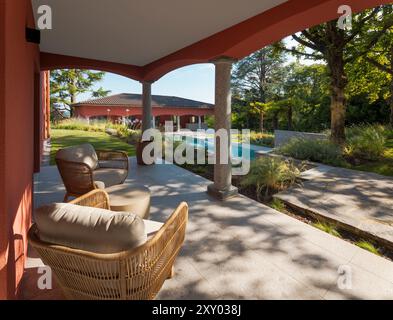 Terrasse einer Villa im Freien, ausgestattet mit zwei Sesseln im Freien und einem kleinen Tisch, perfekt zum Entspannen. Im Hintergrund sehen Sie das Nebengebäude Stockfoto