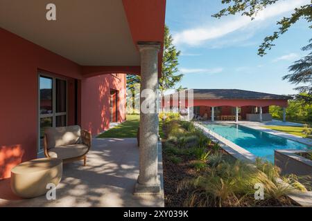 Terrasse einer Villa im Freien, ausgestattet mit Sessel im Freien und einem kleinen Tisch, perfekt zum Entspannen. Im Hintergrund sehen Sie das Nebengebäude und t Stockfoto