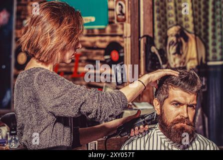 Mann, der Friseur im Friseur besucht. Friseur für Mädchen. Friseurfrau schneidet einen bärtigen Mann in einem Friseurladen Stockfoto