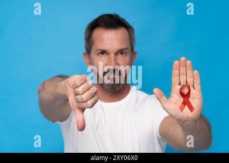 AIDS-Konzept. Der Mann hält ein rotes Band in der Hand und gibt ein Schild mit den Daumen nach unten. Das Bild vermittelt eine Botschaft der Missbilligung oder Meinungsverschiedenheit gegenüber Stockfoto