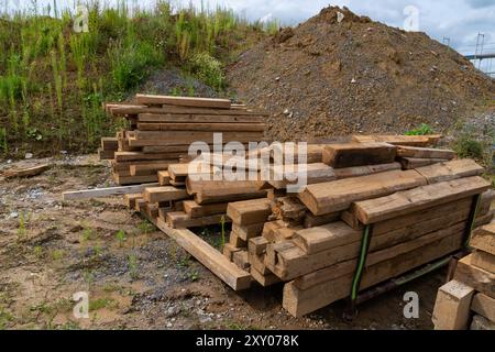 Ein Holzbalkenhaufen liegt auf dem Boden neben einem Kieshügel, umgeben von karger Vegetation. Stockfoto