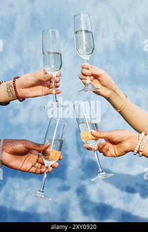 Vier Hände halten Champagner-Gläser in festlichem Toast auf blauem Hintergrund und schaffen eine fröhliche und festliche Atmosphäre Stockfoto