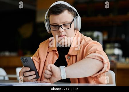 Ein junger Mann mit Down-Syndrom arbeitet ferngesteuert, während er Kopfhörer trägt und seine Smartwatch überprüft. Stockfoto