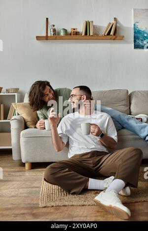 Ein schwules Paar genießt eine Tasse Kaffee und eine Unterhaltung auf dem Wohnzimmerboden. Stockfoto