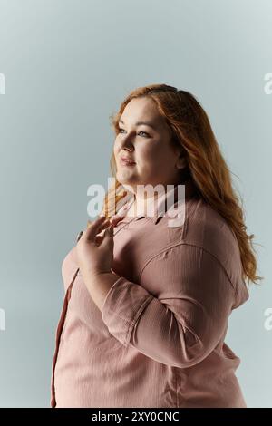 Eine Frau in einem rosafarbenen Hemd steht mit der Hand auf der Brust und blickt mit einem nachdenklichen Ausdruck nach oben. Stockfoto