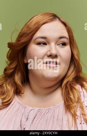 Eine Frau in Übergröße mit rotem Haar sieht aus der Kamera und posiert in einer eleganten rosafarbenen Bluse. Stockfoto