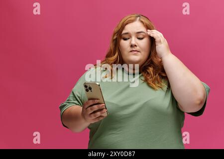 Frau in grünem Hemd mit Telefon vor rosa Hintergrund sieht nachdenklich aus Stockfoto