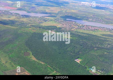 Aus der Vogelperspektive auf einen grünen Wald mit einer Stadt in der Ferne. Blick auf die lebendige Natur und die Stadt von einem Flugzeugfenster aus Stockfoto
