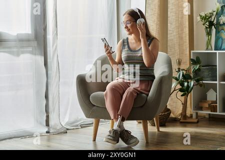 Eine junge Frau mit einer Beinprothese entspannt sich in ihrem modernen Wohnzimmer, hört Musik und scrollt auf ihrem Handy. Stockfoto