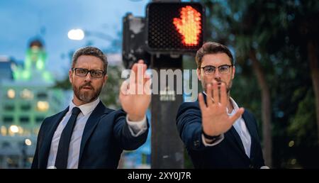 Zwei gutaussehende Geschäftsleute im Anzug hören auf mit der Hand zu singen. Warnausdruck mit negativer und ernsthafter Geste im Gesicht. Halten Sie die Handbewegung an Stockfoto