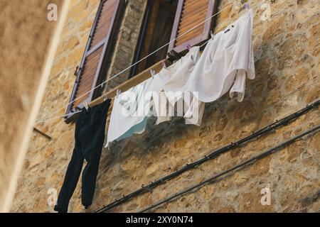 Niedriger Blick auf gewaschene Kleidung, die auf Bademantel trocknet, an der Ziegelmauer vor dem Wohngebäude in der Altstadt der Toskana, Italien Stockfoto
