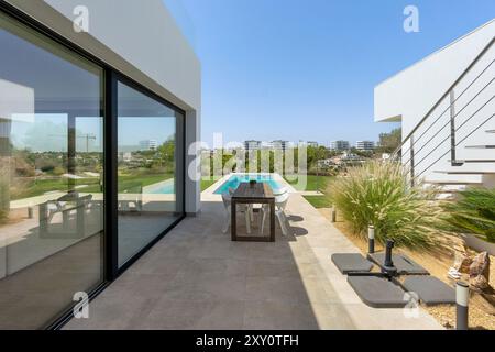 Ein luxuriöses modernes Haus mit weitläufigen Glaswänden, einem unberührten Swimmingpool und einem minimalistischen Terrassenbereich, umgeben von üppigem Grün und Contem Stockfoto