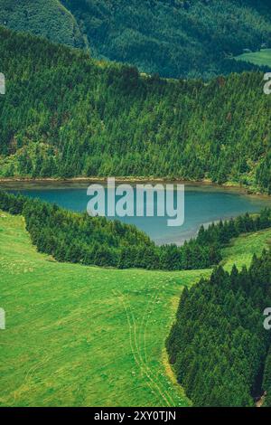 Ein atemberaubendes Luftbild fängt die ruhige Atmosphäre eines kleinen Sees ein, eingebettet zwischen üppig bewaldeten Hügeln der Azoren, dem lebendigen Grün der Th Stockfoto