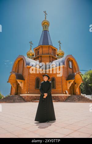 Katholischer Priester, männlich, in traditioneller schwarzer Kleidung gekleidet, stehend vor der reich verzierten orthodoxen katholischen Kirche in Altea, Valencia, Spanien, unter Brig Stockfoto