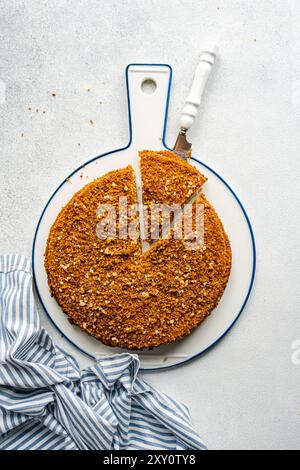 Blick von oben auf einen hausgemachten Honigkuchen, garniert mit Nüssen, serviert auf einem weiß-blauen Servierbrett mit einer gestreiften Serviette. Stockfoto