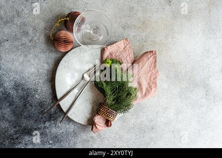 Von oben ein festlicher Weihnachtstisch mit weißer Keramikplatte, silbernem Besteck, rosa Serviette, immergrünen Zweigen und kupferfarbenen Kugeln Stockfoto