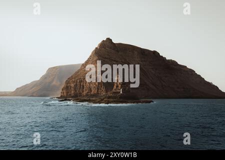 Dieses fesselnde Bild zeigt eine zerklüftete Küstenklippe mit einem kleinen Leuchtturm auf der Basis von Lanzarote, den Kanarischen Inseln, der dramatischen Felsform Stockfoto
