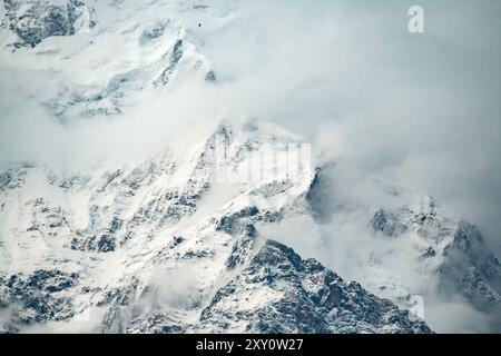 Eine stimmungsvolle Landschaft aus massiven, schneebedeckten Bergen mit hohen Gipfeln, die von weichem Nebel umgeben sind und die vielfältigen Strukturen der Natur hervorheben. Fantastisch Stockfoto