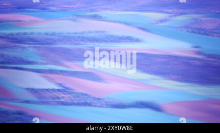 Ein atemberaubendes abstraktes Luftbild, das Bauernfelder zeigt, die mit surrealen Lila-, Blau- und Rosa-Tönen bemalt sind und eine ätherische Landschaft schafft Stockfoto