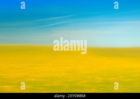 Ein lebendiges abstraktes Bild eines gelben Feldes, das in sanfte Bewegungen verwischt ist, mit einem klaren blauen Himmel über dem Bild, das das Wesen einer ruhigen Landschaft einfängt, Stockfoto