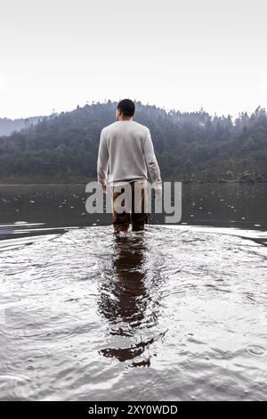 Eine Person, die in einem ruhigen See steht, umgeben von Wald an einem nebeligen Tag, hält einen Moment der Einsamkeit und Reflexion fest Stockfoto