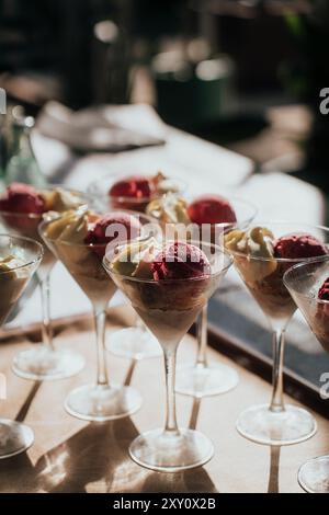 Martini-Gläser, die elegant auf einem gut beleuchteten Tisch angeordnet sind und jeweils mit einer Schaufel farbenfrohen Eiscreme gefüllt sind, bieten eine einzigartige und elegante Dessertoption Stockfoto