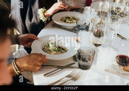 Ein exquisiter Hochzeitstisch mit weißen Porzellanplatten, gefüllt mit Gourmetküche, ergänzt durch eine Auswahl an feinen Weingläsern und raffinierten Tafeln Stockfoto