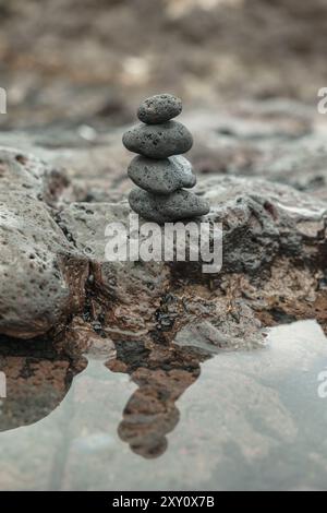 Friedliche Szene aus Zen-Steinen, die sorgfältig in einem Stapel auf einer zerklüfteten felsigen Oberfläche neben einer reflektierenden Wasserpfütze balanciert sind, die Ruhe und balan vermitteln Stockfoto