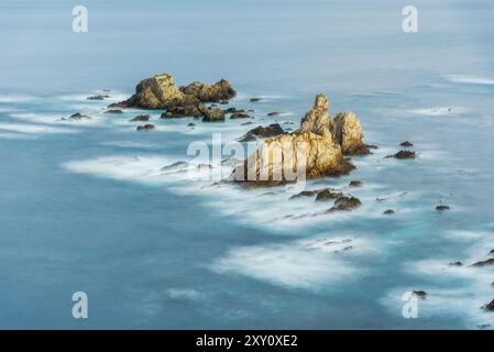 Ein ruhiger Sonnenaufgang beleuchtet den Strand Gueirua in Asturien mit glattem Wasser und markanten Felsformationen. Stockfoto