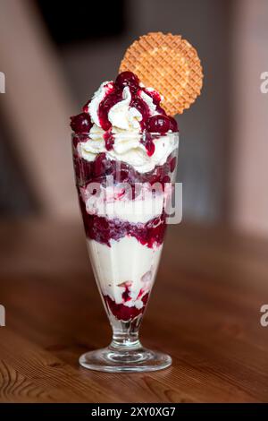 Ein köstlicher Eisbecher mit Kirscheis, serviert in einem hohen Glas, garniert mit Schlagsahne und Waffelkeks, perfekt für süße Leckereien. Stockfoto