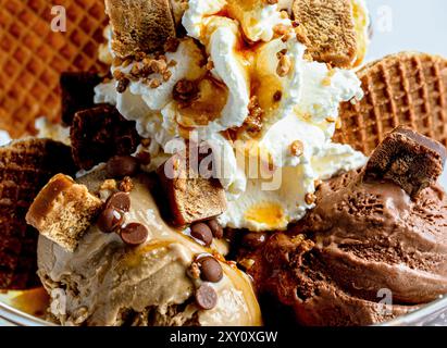 Ein verführerischer Eisbecher mit Kugeln mit reichhaltiger Schokolade und Karamelleis, garniert mit Schlagsahne, Karamellsauce, Schokoladenchips und c Stockfoto