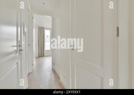 Ein leerer, gut beleuchteter Korridor mit Hartholzböden führt zu einem luftigen Zimmer mit Zugang zum Balkon mit weißen Wänden und Türen. Stockfoto