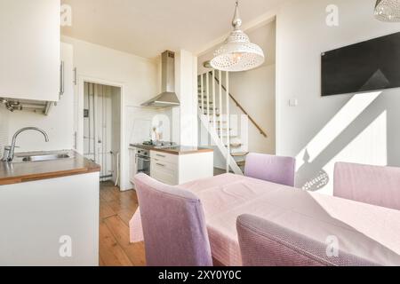 Heller und luftiger Blick auf eine moderne Küche mit Holzfußboden, der zu einem Essbereich mit rosafarbener Tischdecke und Stühlen führt. Stockfoto