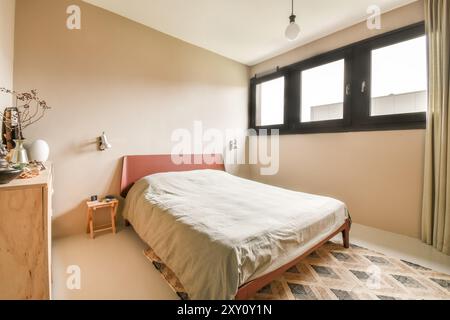 Ein gemütliches, minimalistisches Schlafzimmer mit rosafarbenem Bettgestell, neutraler Bettwäsche, einer Glühbirne und einem gemusterten Teppich unter dem Fuß, beleuchtet durch natürliches Licht Stockfoto