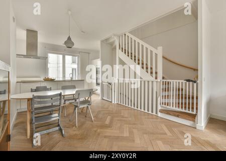 Eine geräumige, moderne Küche mit Esstisch, Stühlen und einer Holztreppe, die in die obere Etage führt, mit viel Tageslicht. Stockfoto