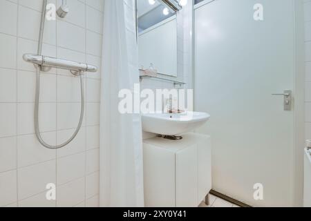 Modernes Bad mit weißem Standwaschbecken, Dusche mit Vorhang und hellen gefliesten Wänden. Stockfoto