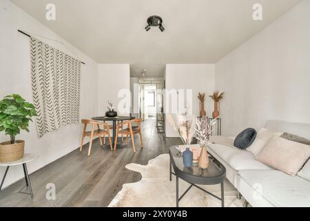 Ein einladendes, modernes Wohnzimmer mit minimalistischer Einrichtung, komfortablem Sofa, Esstisch aus Holz und dekorativen Pflanzen, die die gemütliche Atmosphäre unterstreichen Stockfoto