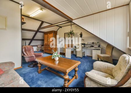 Ein traditionelles Home Office in einem Dachgeschoss mit Holzbalken, klassischen Möbeln und blauem Teppichboden. Stockfoto