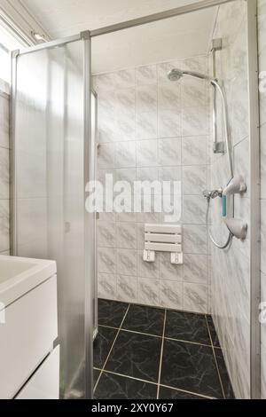 Das helle, moderne Badezimmer verfügt über eine Duschkabine aus Glas, marmorähnliche Wandfliesen und stilvolle schwarze Bodenfliesen. Stockfoto