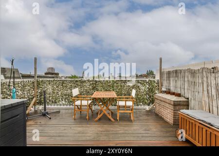 Eine gemütliche, urbane Dachterrasse mit Holztisch und Stühlen vor einer mit Efeu bedeckten Wand unter blauem Himmel. Stockfoto